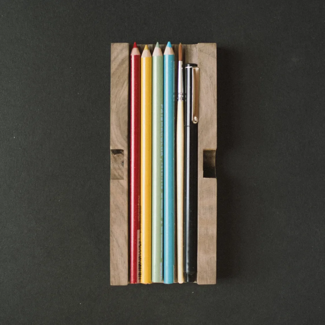 Wooden tray containing colored pencils, a brush and a pen