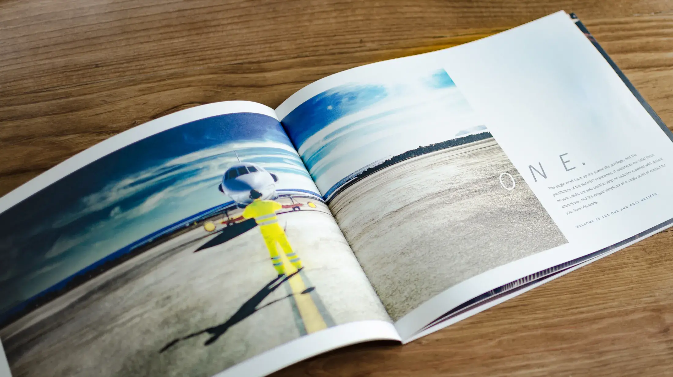 full span of open book, page titled "O N E." with focus on image of jet on runway spilling across the pages 