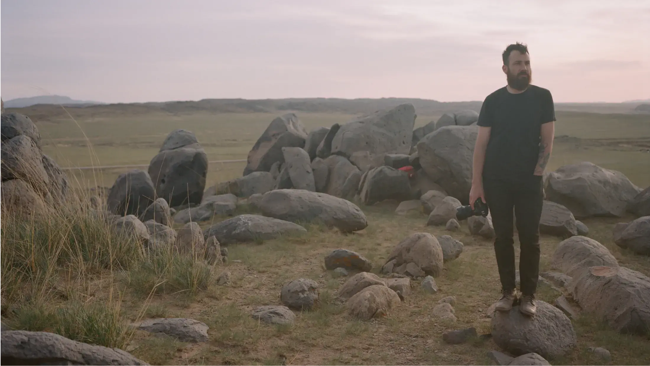 man surrounded by boulders in an open field with a camera by his side