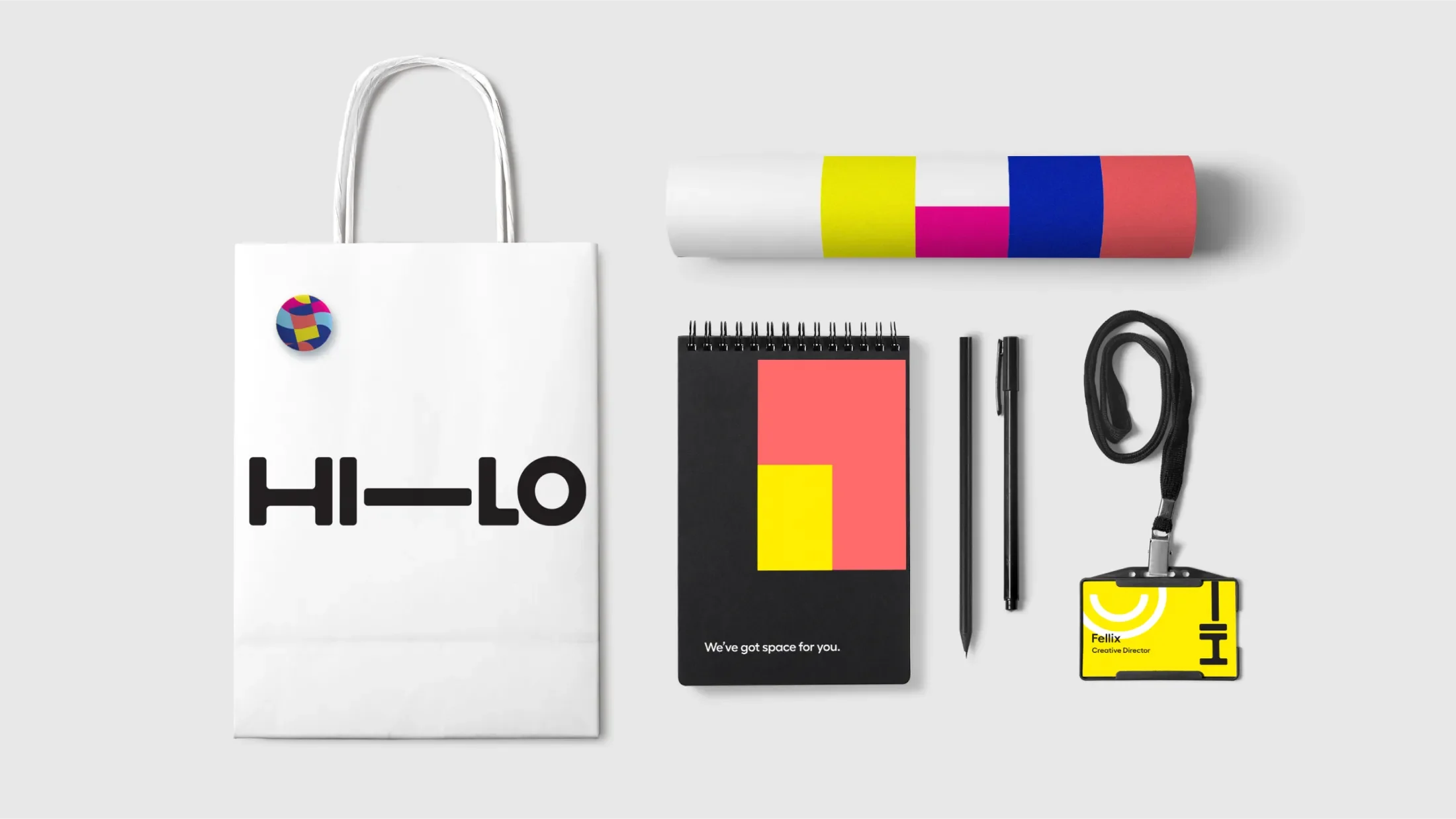 Spread of Hi-Lo themed stationary, including a bag, notepag, namebadge, pens, colored tube and a button