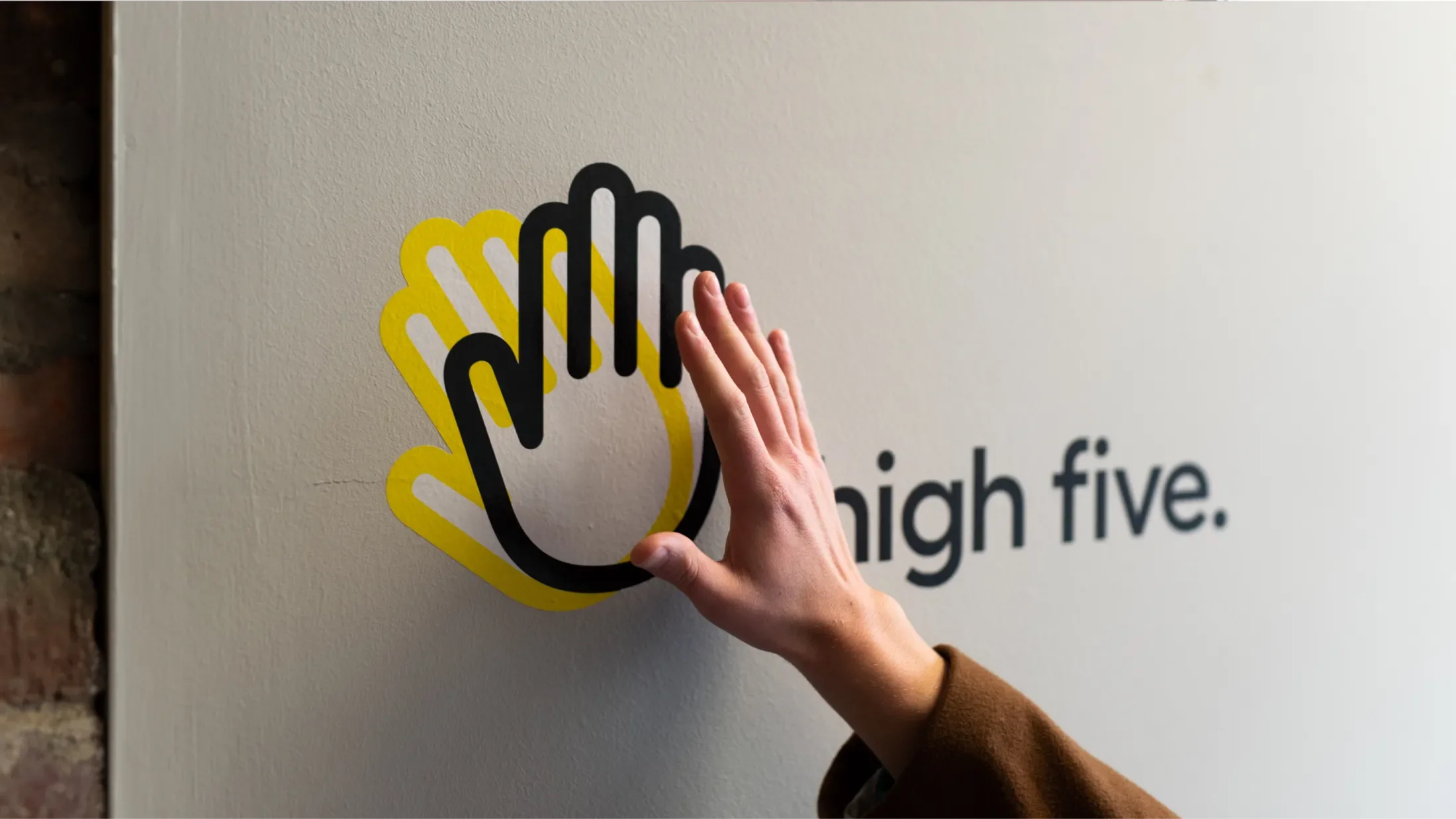 Hand touching a wall graphic of a black and a yellow hand crossing next to "high five."