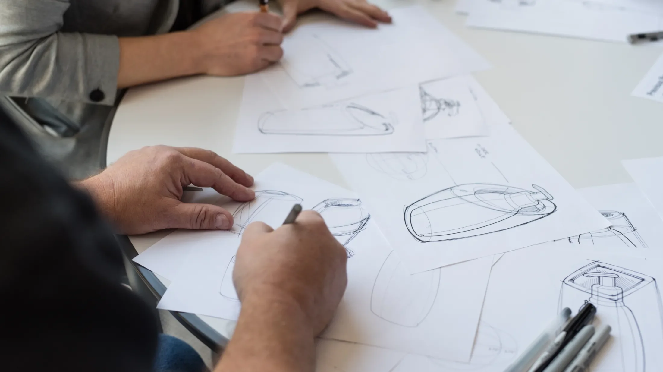 Two people sketching designs for a bottle holder