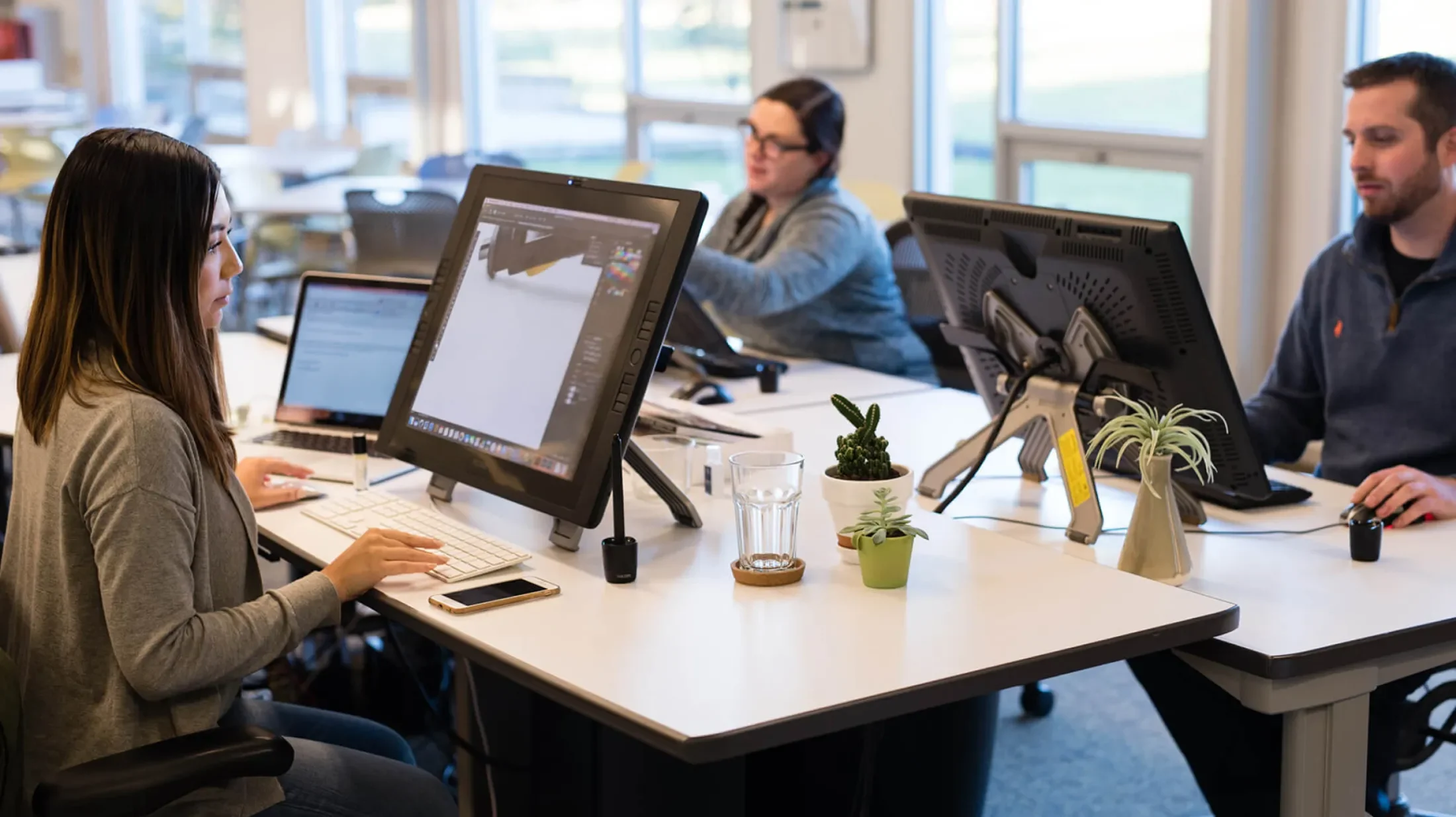 Three people at adjacent desks working on design tablets