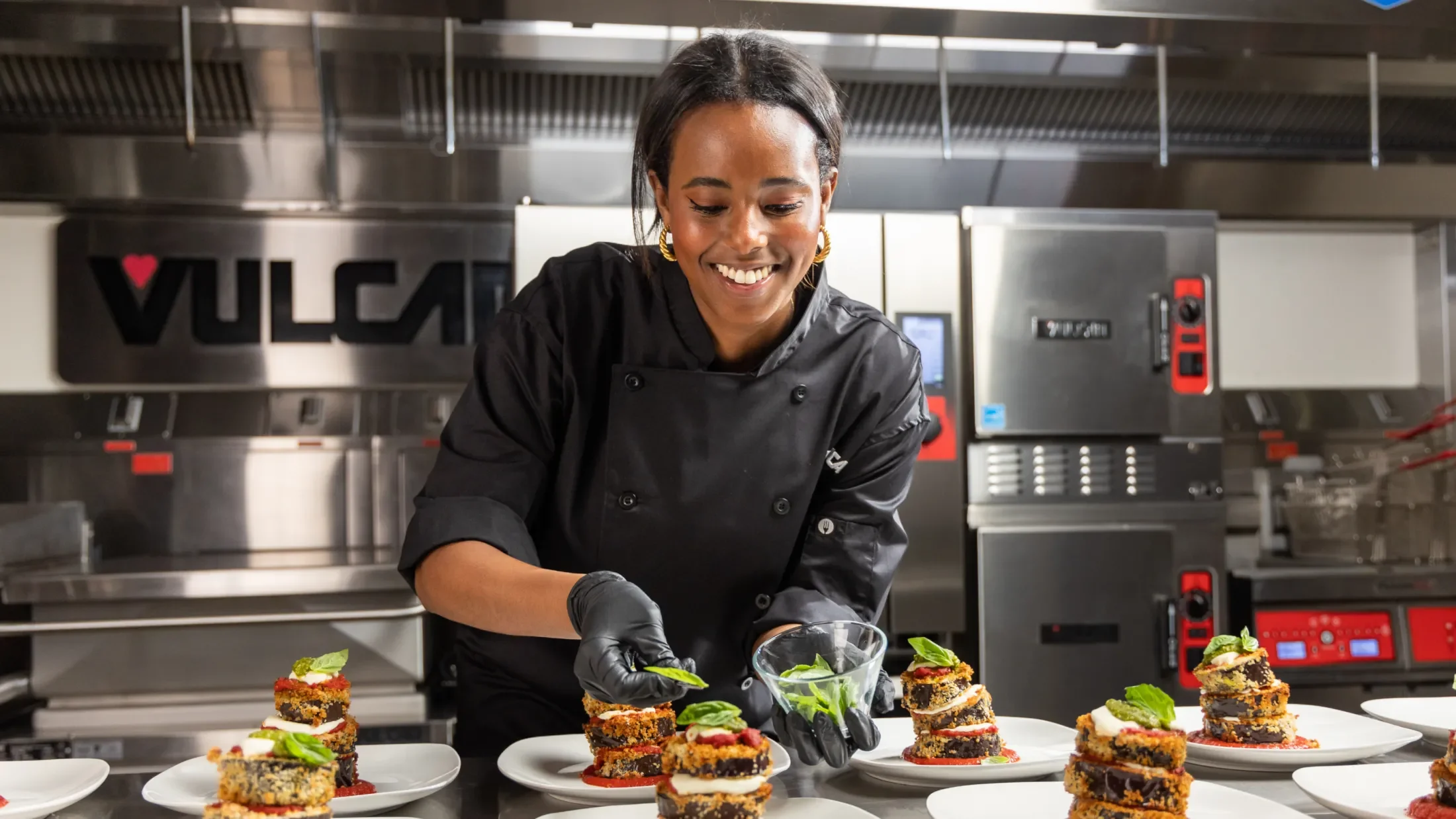 Smiling chef in a Vulcan kitchen plating several identical dishes